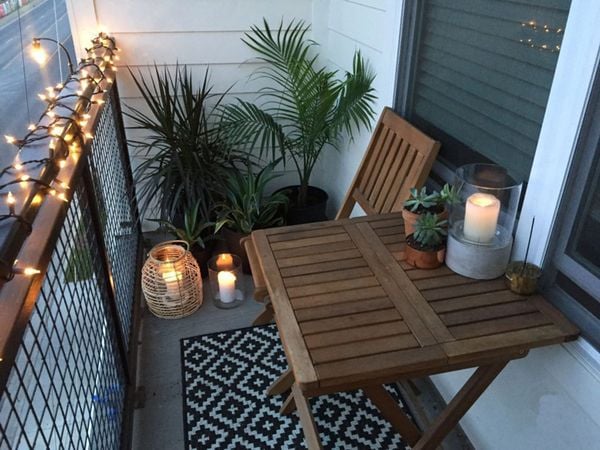 Ban công nhỏ bố trí bàn gỗ, cây xanh và hệ thống đèn trang trí tạo ánh sáng ấm