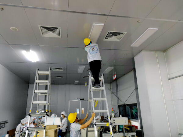 Công nhân đang lắp giá đỡ và cố định đèn trong quá trình thi công chiếu sáng nhà xưởng